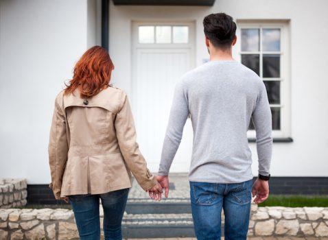 Couple holding hands in front of their new home.