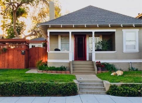 Exterior of a small cottage style house with porch and pet dog on manicured front lawn