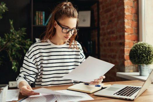 woman holding paper working on laptop