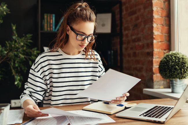 woman holding paper working on laptop
