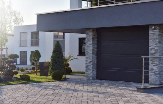 Garage of a modern house with an automatic door next to garden plants.